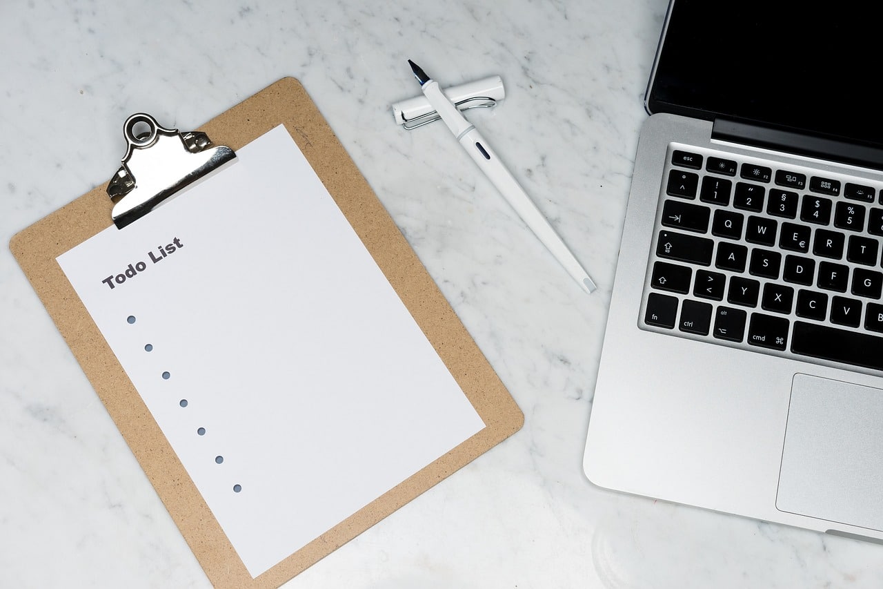 Clipboard with a blank to-do list beside a laptop and pen on a marble desk